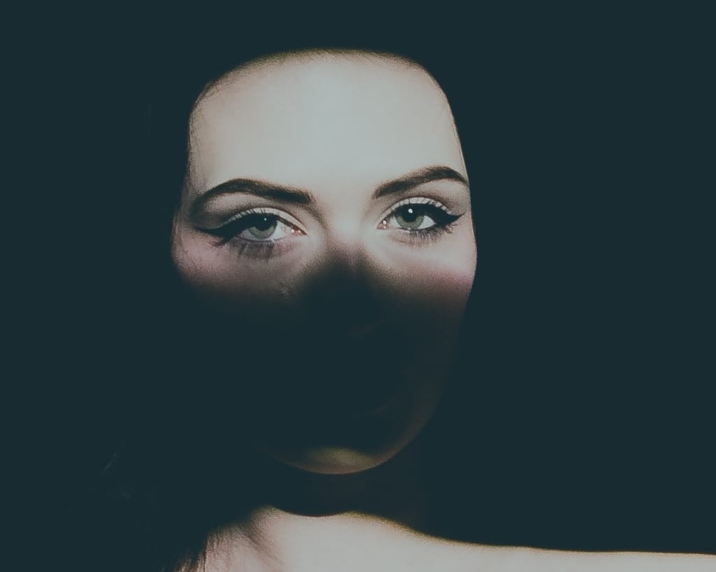 Close-up portrait of Lana West with dramatic, low-key studio lighting highlighting her eyes.