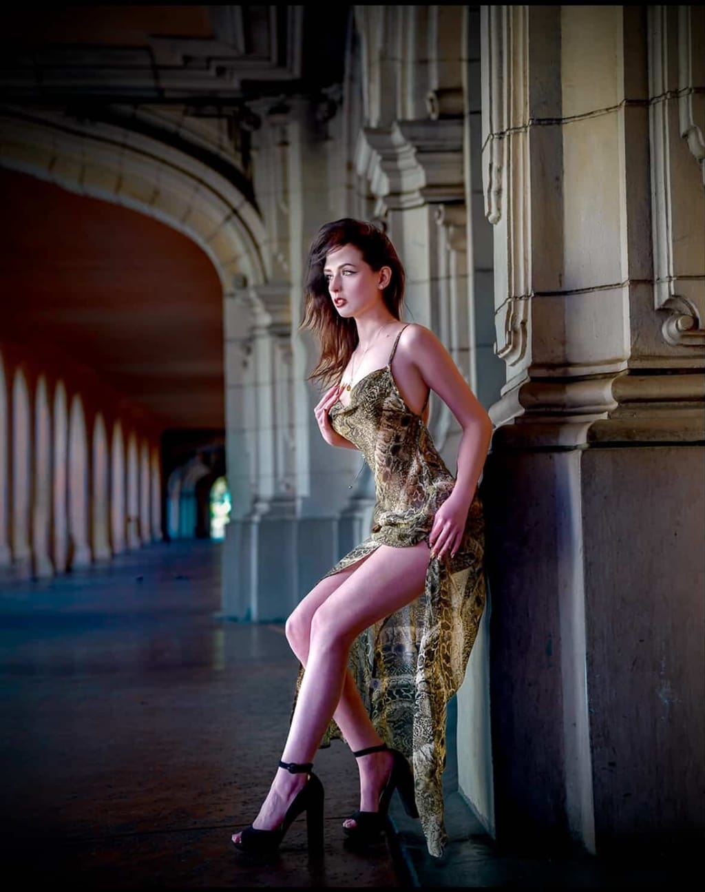 Lana West in an animal-print slip dress posing in a stone colonnade.