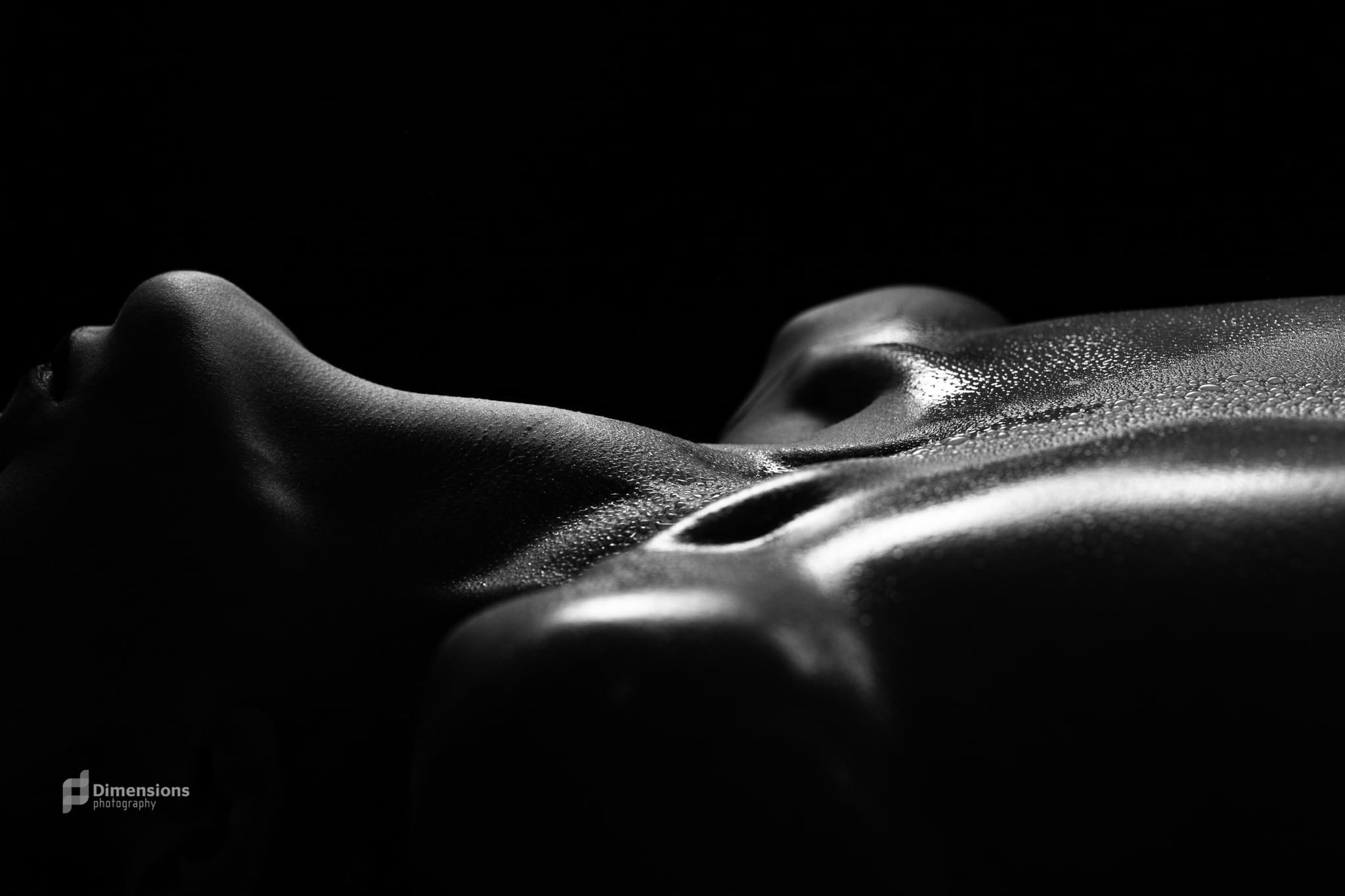 Black-and-white fine-art close-up of skin and light with water droplets, a studio artistic-nude study.