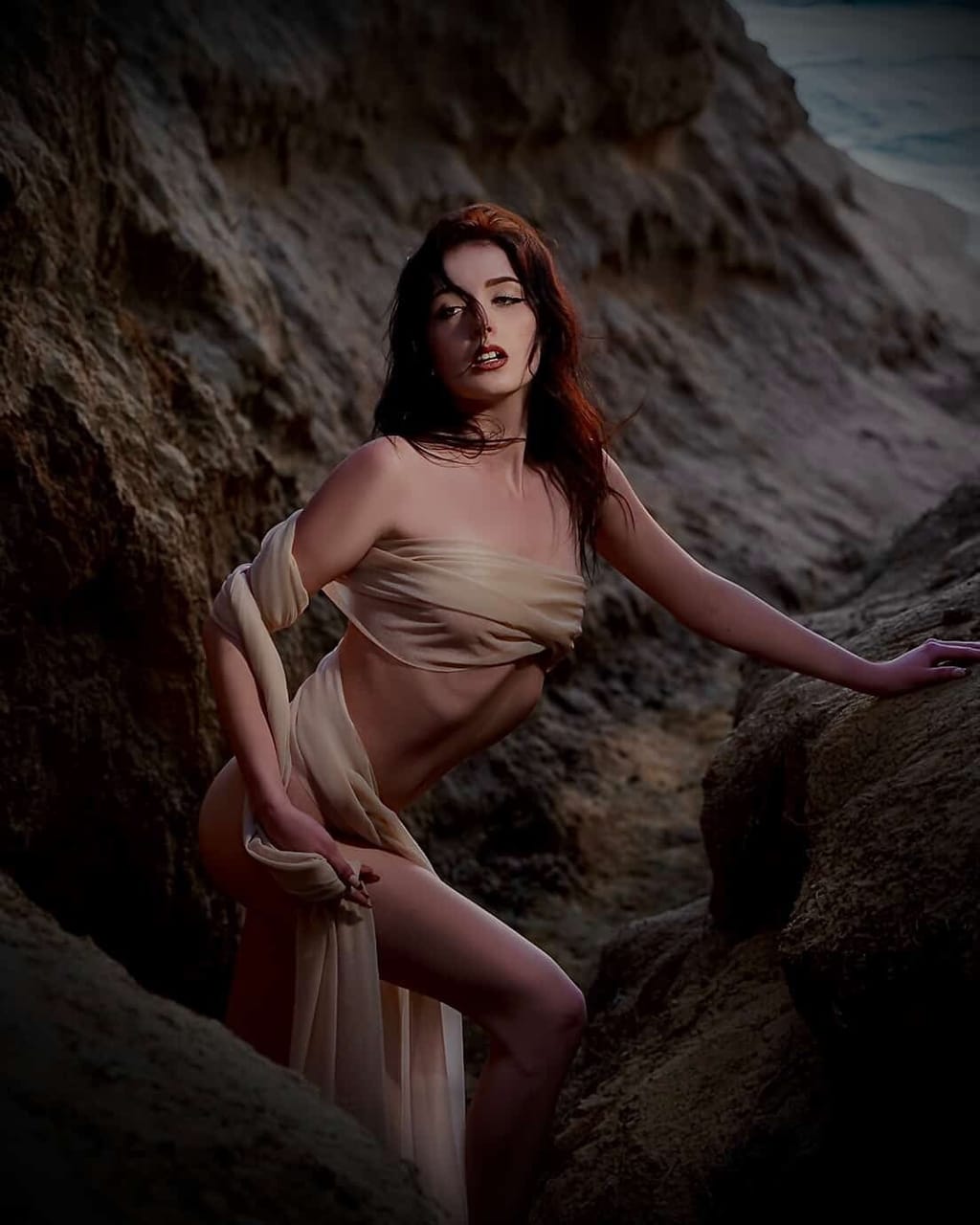 Lana West in a draped fabric wrap posing among sandstone rock formations for an artistic editorial shoot.
