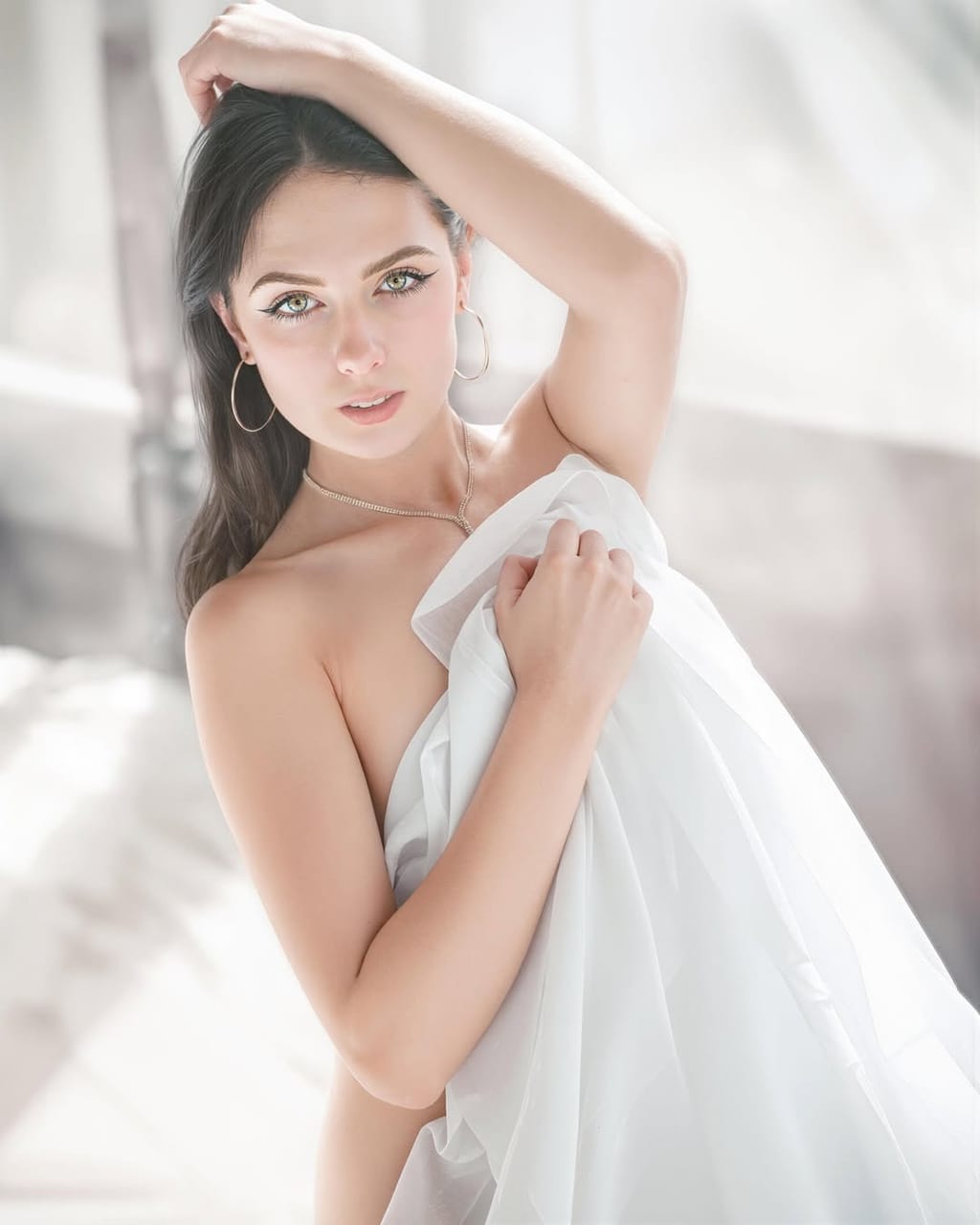 Lana West wrapped in a sheer white drape with one shoulder bare, softly lit indoor boudoir portrait.