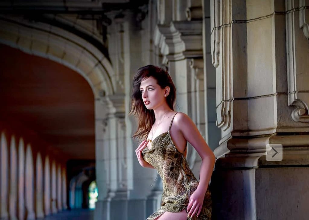 Editorial photo of Lana West in a snake-print dress posing in a stone colonnade.
